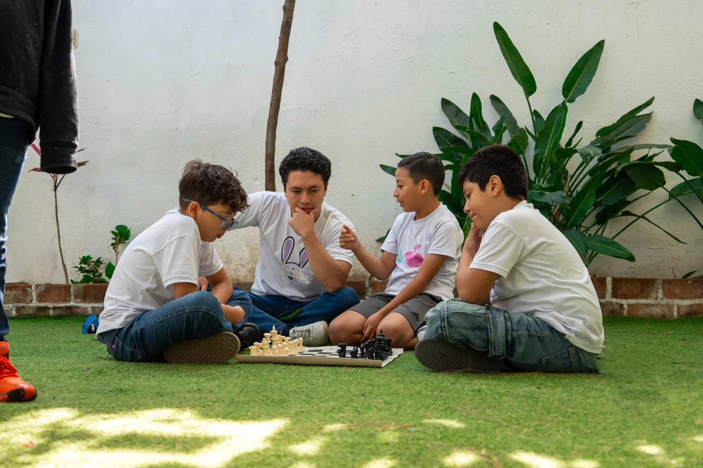 Profesor sentado en el patio enseñando ajedrez a tres alumnos