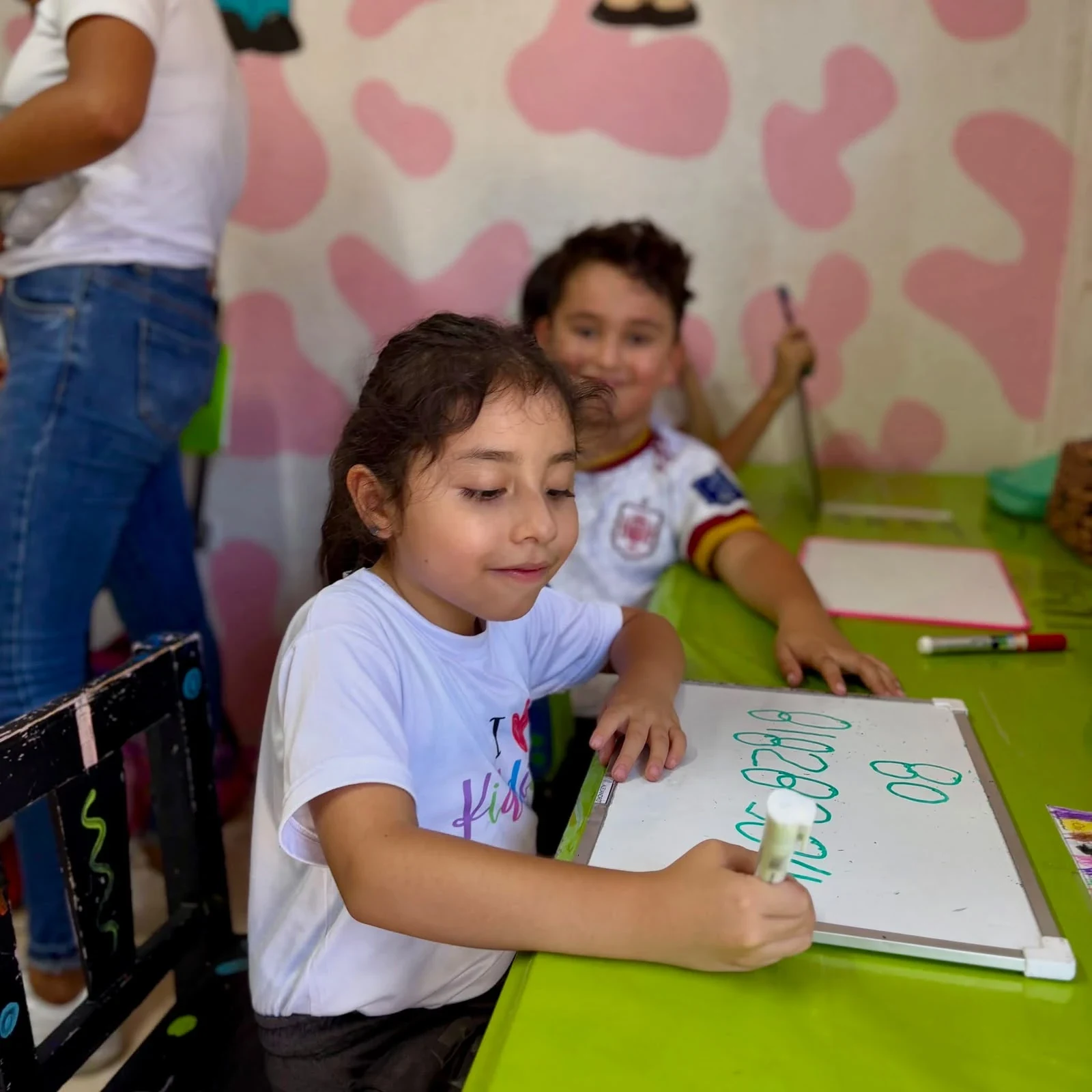 Alumna de Kiddies Club sonriendo mientras escribe números en su pizarra en el salón
