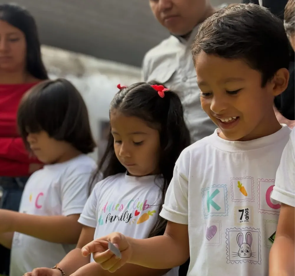 Niños de Kiddies Club sonriendo mientras trabajan en una actividad con sus familias durante las Aulas abiertas