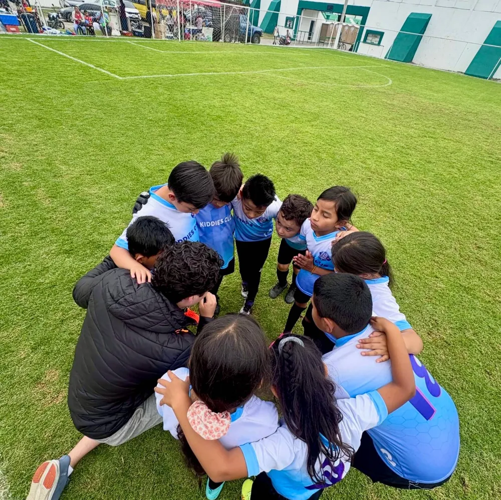 Niños de Kiddies Club abrazados en círculo con su entrenador antes de un partido