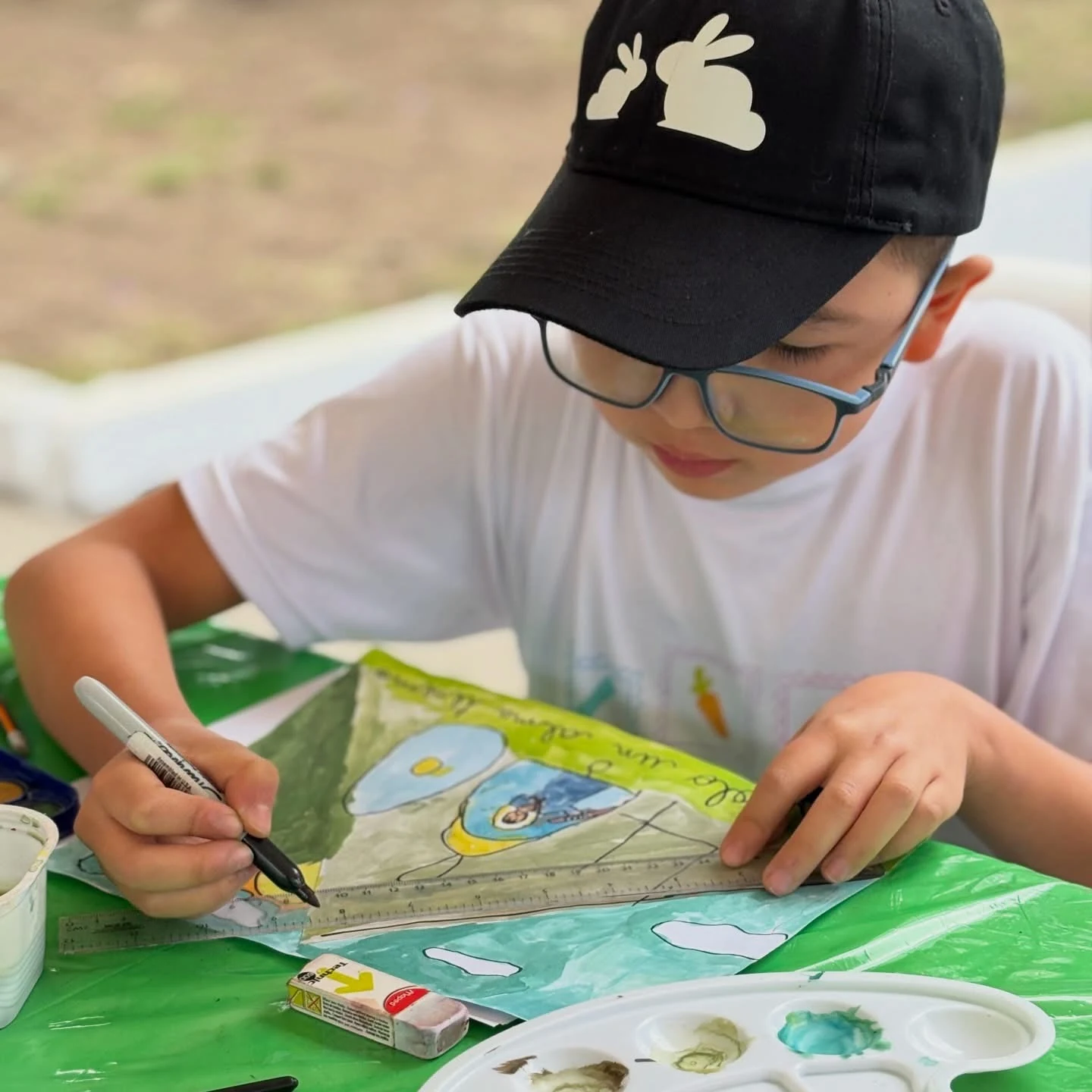 Alumno de Kiddies Club con gorra y lentes terminando su pintura con marcador y regla